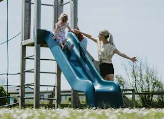 A child going down the slide at our adventure playground at Newperran Holiday Park. There is a woman standing next to the slide. image