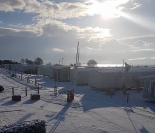 A view over our stunning holiday homes at Mersea Island, Essex, on a snowy winters day. The winter sun is shining in the background.