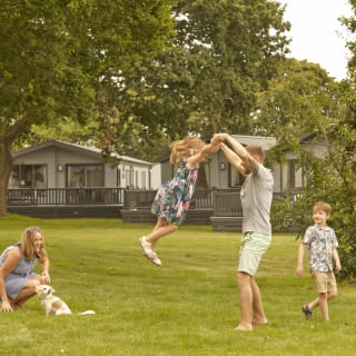A young family playing outside on a sunny day. There is a row of caravans in the background. image