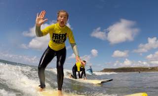 A girl surfing in the sea whilst waving at the camera. image