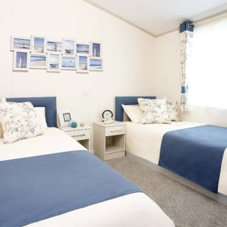 The interior of one of our Luxury holiday lodges. There's a twin bedroom with side tables and photos on the wall.