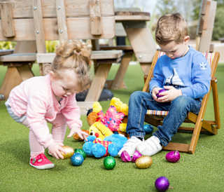 Two kids enjoying Easter activities at one of our holiday parks. They are both sitting down playing with colourful Easter eggs on the floor.