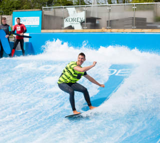 A young male is surfing on a wave stimulator with two other males watching from the sideline. image