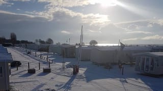 A view over our stunning holiday homes at Mersea Island, Essex, on a snowy winters day. The winter sun is shining in the background.