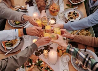 A group of people cheersing over a table of food. image