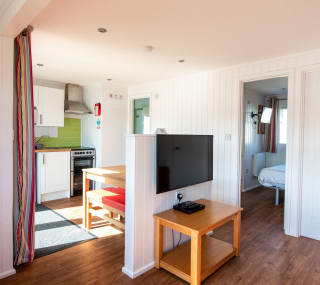 The interior of one of our holiday home Chalets. There’s a large TV, double bedroom, and kitchen space. There are bright colours in the holiday home. image