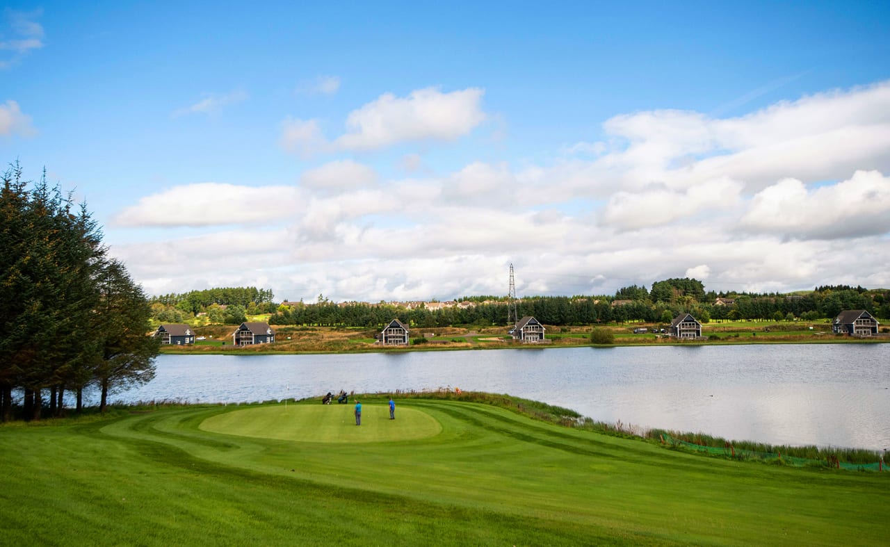 A view of the golf course at our stunning Scottish resort, Piperdam, on a cloudy but sunny day. There are views of lodges in the distance overlooking the lake and golf course. image