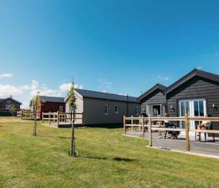 A bright sunny day at our static caravan holiday park in Bay Filey, Yorkshire. In the photo is a row of wooden static caravans next to a grass communal lawn.