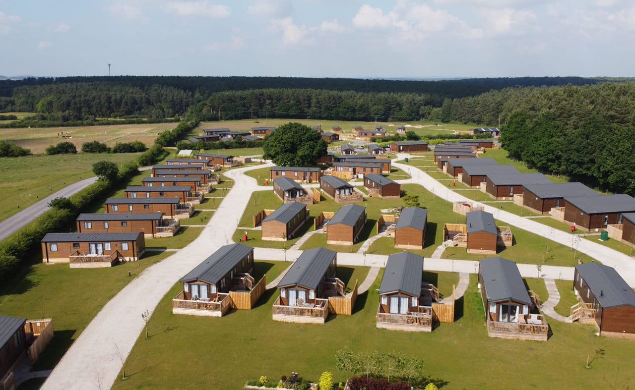 Drone footage above our stunning resort Clumber Park, Nottinghamshire. There are rows of wooden holiday homes perched within stunning woodland scenery. image