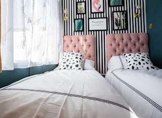 A single bed with cow spot print and light pink duvet covers and pillow. The wall behind it has black and white thin stripes. image