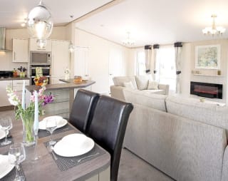 The interior of one of our Luxury holiday lodges. There's a dining area, kitchen section, and two grey sofas.