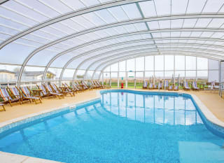 The awesome indoor swimming pool at our holiday park in Essex, Mersea Island. There are multicoloured deck chairs all around the pool. image