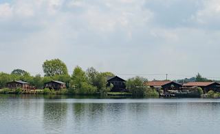 A panoramic view of a river with wooden lodges and trees at one of our holiday parks in Lincolnshire. image