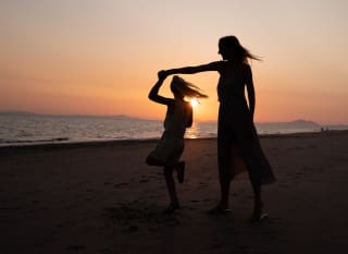 A mother and daughter dancing on the beach at sunset. image