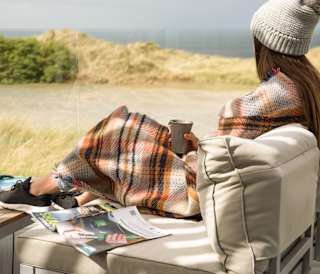 A lifestyle image of a woman relaxing on the decking at our stunning holiday park in Cornwall, St Ives Bay. There are views of the ocean in the background.