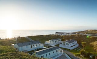 Two rows of caravans with views of the sea and the sun setting at our holiday park in North Wales, Barmouth Bay. image