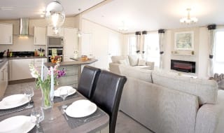 The interior of one of our Luxury holiday lodges. There's a dining area, kitchen section, and two grey sofas. image