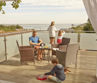 A family of four on the balcony of their holiday home in The Bay Colwell. There are two adults, a young boy, and a young girl with strawberry blonde hair, and all dressed in summer attire.