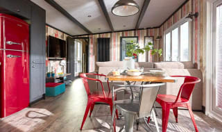 An image of the interior of one of our holiday lodges. There's wooden panneling, a cream fabric sofa and red metal dining chairs around a wooden table. image
