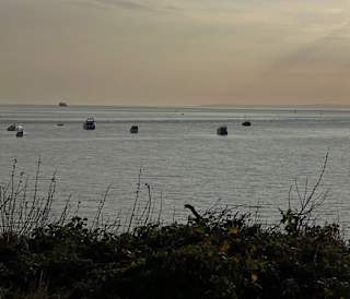 A sunset on the beach in The Bay Colwell. The sun is drifting down and the light is spread across the sea view. There are four boats in the near distance, and another four much farther out.