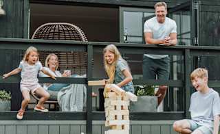 A family of five playing a game of jenga outside their accommodation. image