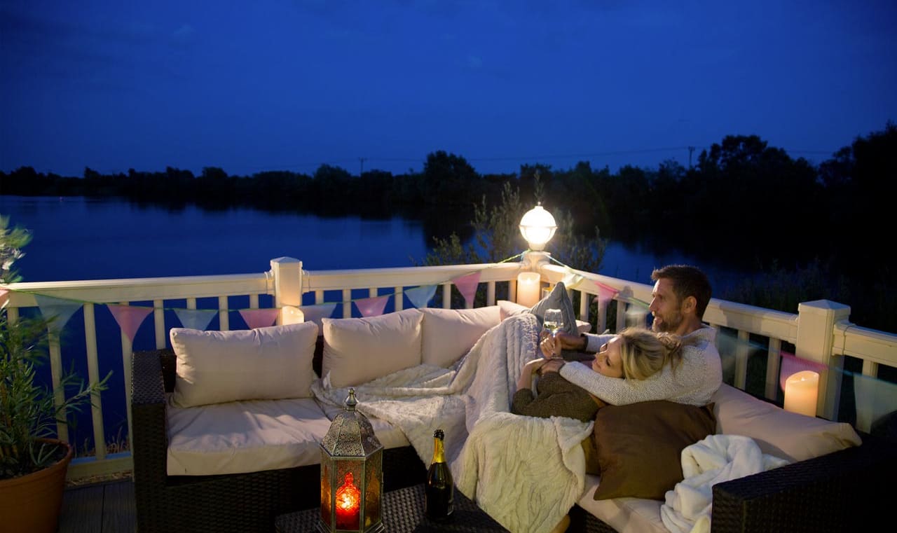 A couple cuddling on the decking of our holiday homes overlooking a lake. image