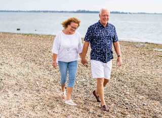 A mature hetero white couple are walking along the sands of Mersea Island beach, Essex. image