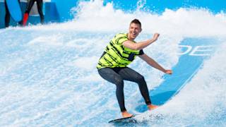 A young male is surfing on a wave stimulator with two other males watching from the sideline.