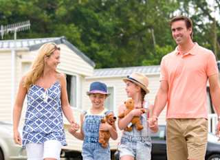 A family holding hands walking through one of our stunning holiday pars. There is a row of caravans in the background. image