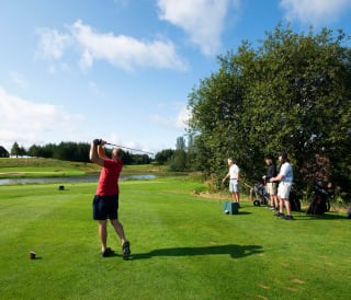 A group of people playing golf on a sunny, cloudy day at Piperdam, Scotland.