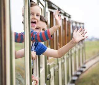 Two children waving at the camera out the window of a train.