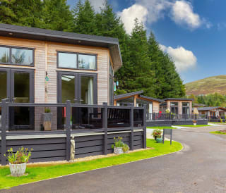 A view of the exterior of our stunning holiday homes for sale at Glendevon Residential Country Park, Scotland. There is a row of wooden lodges and views in the background of the stunning surrounding scenery.
