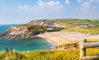 An image of Church Cove, Cornwall on a summers day. There are views of the beach, blue sea and surrounding greenery. image