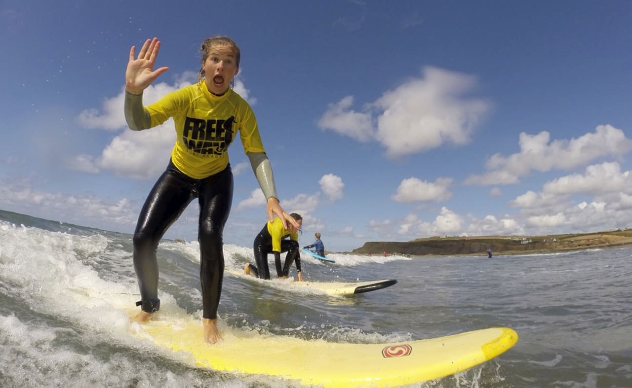 A girl surfing in the sea whilst waving at the camera. image
