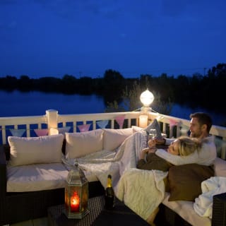 A couple cuddling on the decking of our holiday homes overlooking a lake. image