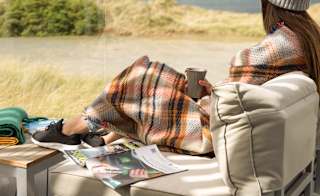 A lifestyle image of a woman relaxing on the decking at our stunning holiday park in Cornwall, St Ives Bay. There are views of the ocean in the background. image