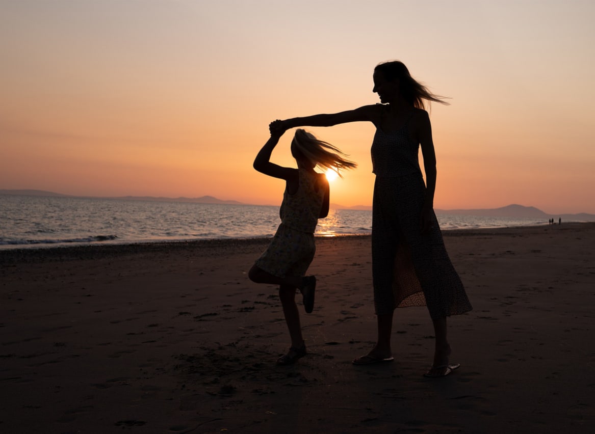 A mother and daughter dancing on the beach at sunset. image