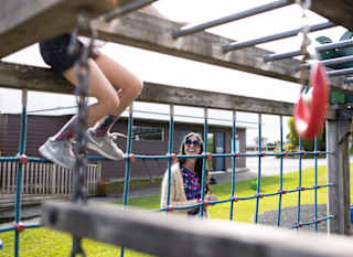 A young mum is watching her child climb the playground climbing frame. image