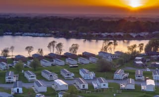 An arieal photoof a holiday park at Tattershall Lake, Lincolnshire. The sun is setting over the horizon and the park has holiday lodges in neat rows by the river. image
