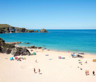 An aerial view of Padstow beach. Holiday goers are on the beach and in the sea. A bright blue sky is above the sea.