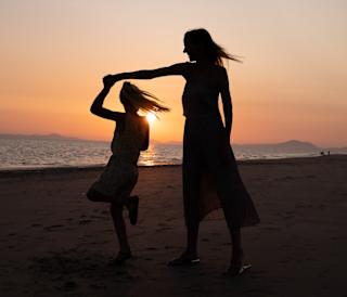 A mother and daughter dancing on the beach at sunset.