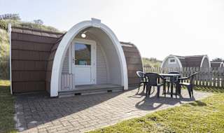 Exterior of our camping pod at St Ives Bay, Cornwall. A table and chair is located on the right, the perfect spot for brunch in the sunshine. image