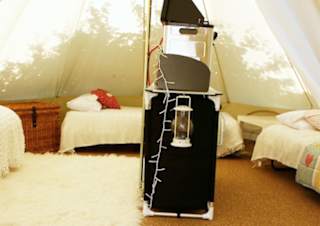 A photo of the living space of a canvas bell tent. There is a brown woven floor mat and on top of this is a white faux fur rug. There is seating arranged in a semicircle.
