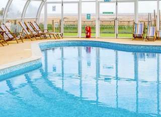 The awesome indoor swimming pool at our holiday park in Essex, Mersea Island. There are multicoloured deck chairs all around the pool. image