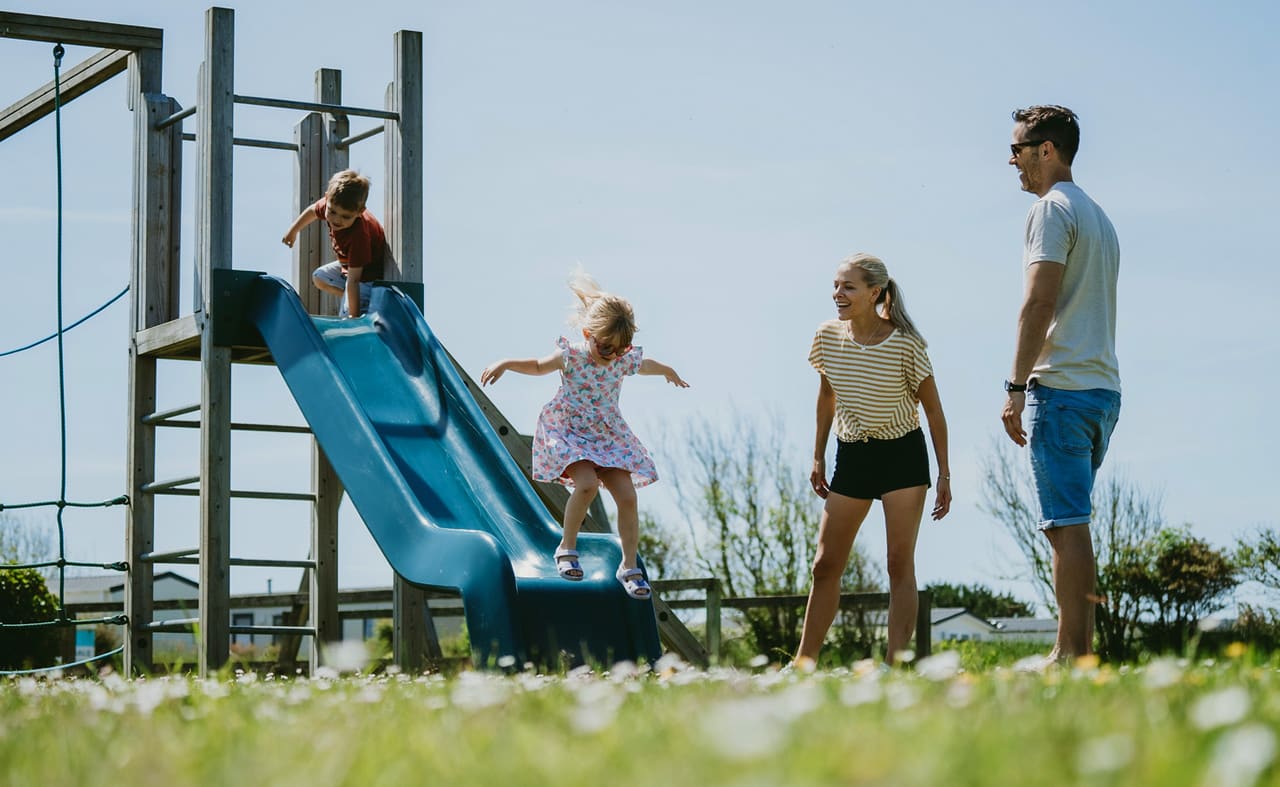 A young family playing in the adventure playground at our holiday park in Cornwall, Newperran. There are two children and a mother and father. image