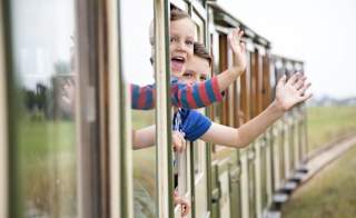 Two children waving at the camera out the window of a train. image