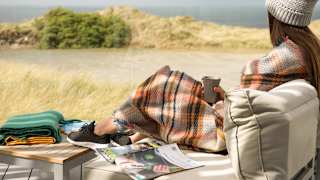 A lifestyle image of a woman relaxing on the decking at our stunning holiday park in Cornwall, St Ives Bay. There are views of the ocean in the background.
