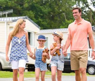 A family holding hands walking through one of our stunning holiday pars. There is a row of caravans in the background.