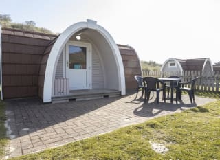 Exterior of our camping pod at St Ives Bay, Cornwall. A table and chair is located on the right, the perfect spot for brunch in the sunshine. image