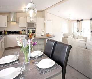 The interior of one of our Luxury holiday lodges. There's a dining area, kitchen section, and two grey sofas.